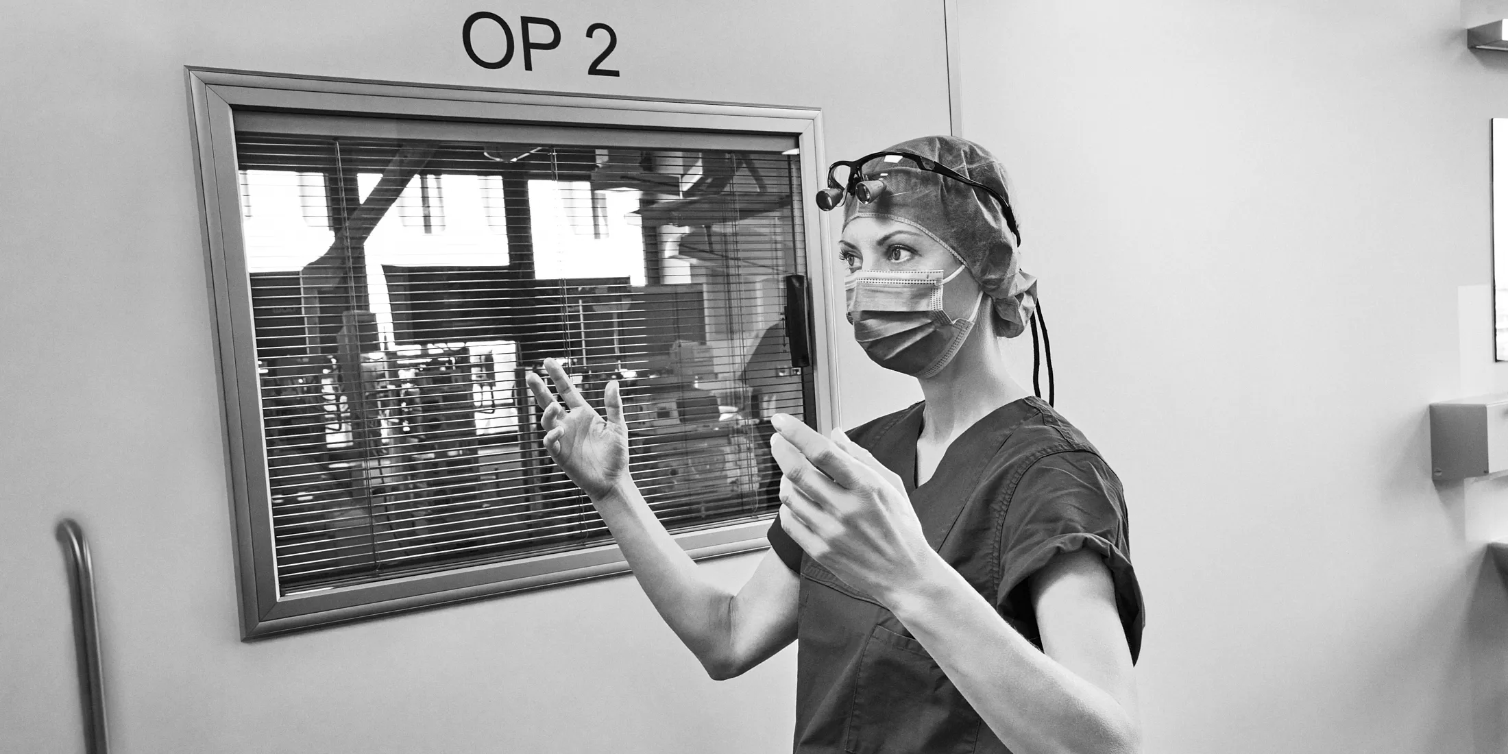 Die beeindruckende Chirurgin Dr. med. Nina Picker steht vor dem Operationssaal, ihre langen muskulösen Arme erhoben.